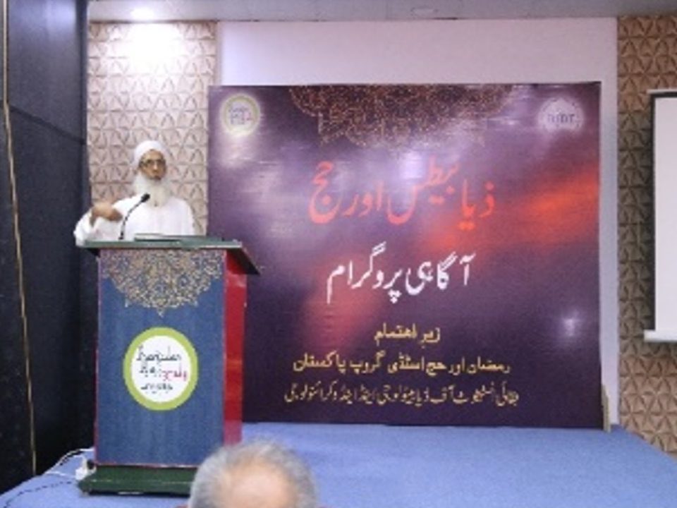 A senior speaker at the podium in front of a banner in Urdu reading Diabetes and Hajj awareness programme
