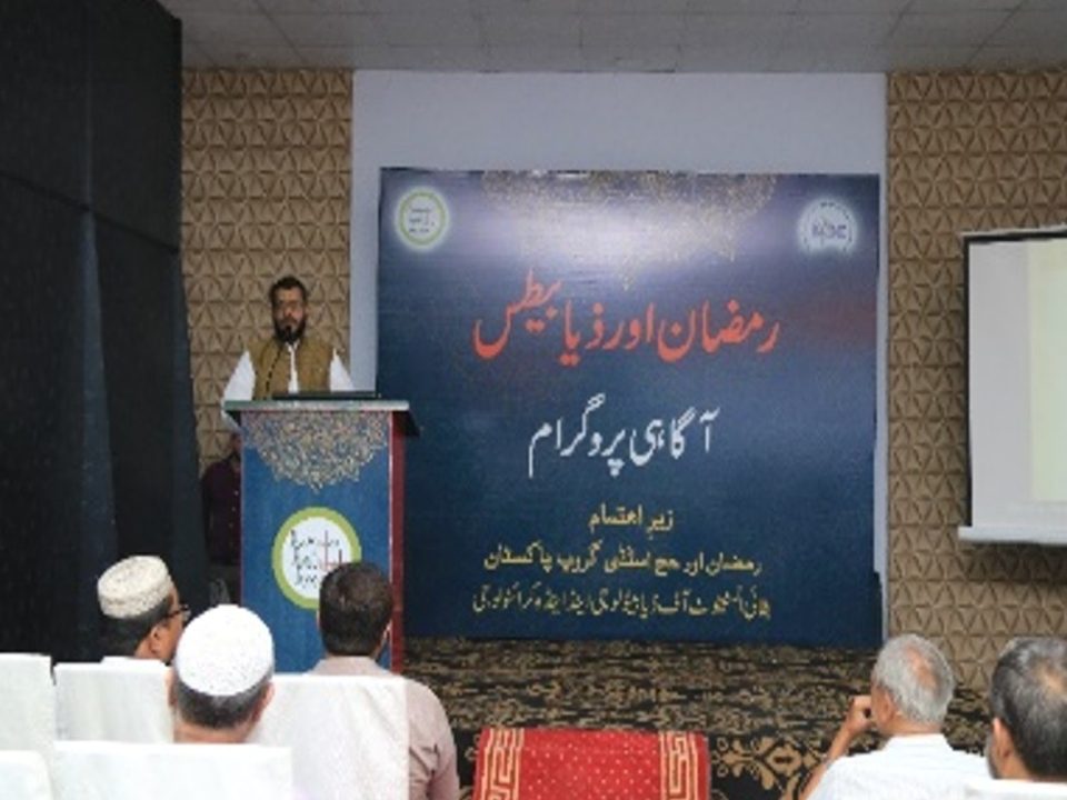 A speaker at the podium in front of a banner in Urdu reading Ramadan and diabetes awareness programme